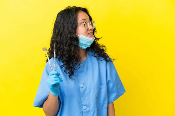 年轻的亚洲牙医在孤立的背景下拿着工具 看着旁边 微笑着 — 图库照片