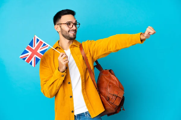 Young caucasian man holding an United Kingdom flag isolated on yellow background giving a thumbs up gesture