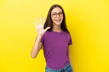 Sarı arka planda izole edilmiş genç bir Fransız kadın parmaklarıyla beşi sayıyor.