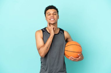Basketbolcu Afro-Amerikan bir adam mavi arka planda izole edilmiş, yukarı bakarken bir fikir düşünüyor.