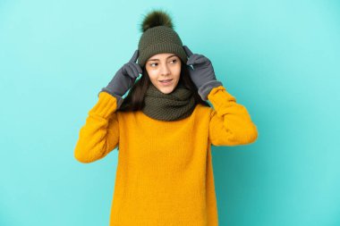 Genç Fransız kız mavi arka planda izole edilmiş, kışlık şapkalı, kuşkulu ve düşünceli.