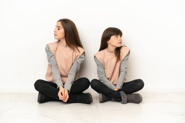 Beyaz arka planda izole edilmiş yerde oturan küçük kardeşler gergin ve korkmuş.