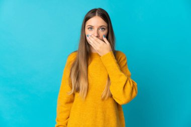 Genç Litvanyalı kadın mavi arka planda izole edilmiş, ağzı elle kapatılmış.