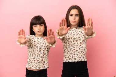 Pembe arka planda izole edilmiş küçük kız kardeşler hayal kırıklığı için dur hareketi yapıyorlar.