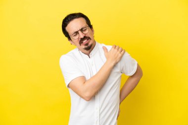 Genç, beyaz bir adam sarı arka planda izole edilmiş. Omuz ağrısı çekiyor. Çabaladığı için.