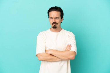 Mutsuz bir ifadeyle mavi arka planda izole edilmiş genç beyaz bir adam.