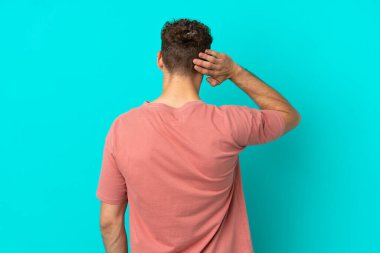 Genç yakışıklı beyaz adam mavi arka planda izole edilmiş ve düşünüyor.