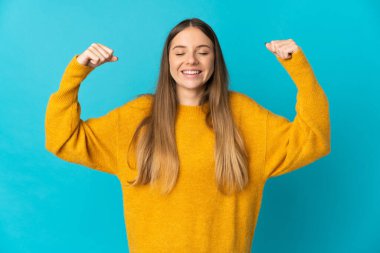 Genç Litvanyalı kadın mavi arka planda izole edilmiş, güçlü bir jest yapıyor.
