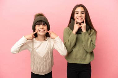 Pembe arka planda izole edilmiş, mutlu ve hoş bir ifadeyle gülümseyen küçük kız kardeşler.