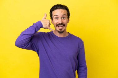 Sarı arka planda izole edilmiş genç beyaz bir adam telefon jesti yapıyor. Bana geri dönüş işareti ver.