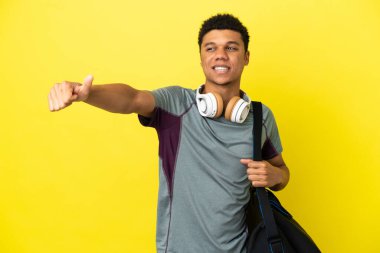 Young sport African American man with sport bag isolated on yellow background giving a thumbs up gesture
