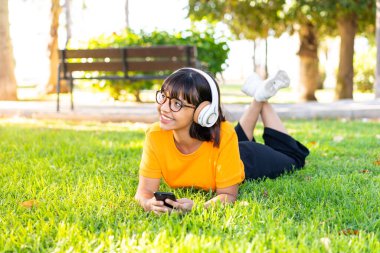 Genç esmer kadın açık havada cep telefonu ve mutlu müzik dinliyor.