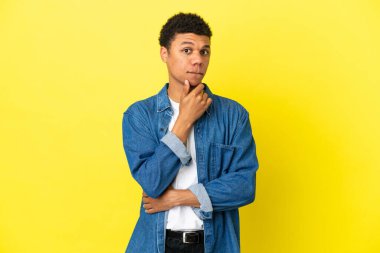 Genç Afrikalı Amerikalı adam sarı arka planda izole edilmiş. Şüpheleri ve düşünceleri var.