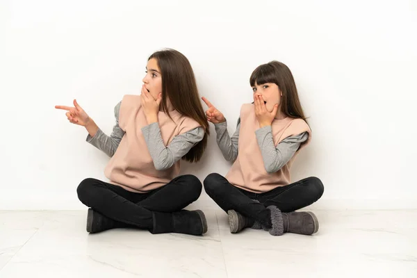 Little Sisters Sitting Floor Isolated White Background Pointing Finger Side — Stock Photo, Image