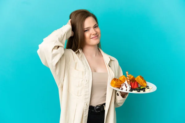 Adolescente Menina Segurando Waffles Sobre Isolado Fundo Azul Com Dúvidas — Fotografia de Stock