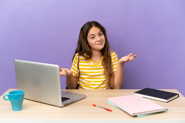 Little student girl in a workplace with a laptop isolated on purple background happy and smiling