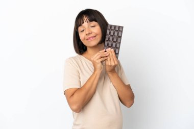 Genç melez hamile kadın beyaz arka planda izole edilmiş çikolata tableti alıyor ve mutlu.