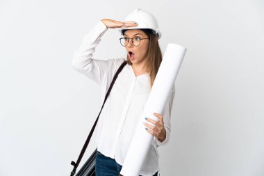 Young Lithuanian architect woman with helmet and holding blueprints isolated on white background doing surprise gesture while looking to the side