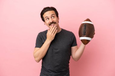 Genç beyaz adam pembe arka planda izole edilmiş rugby oynuyor gülümserken yukarı bakıyor