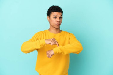 Young African American man isolated on blue background making the gesture of being late