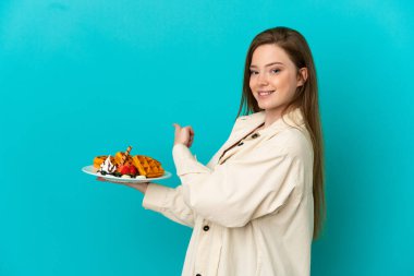 İzole edilmiş mavi arka planda waffle tutan genç kız.