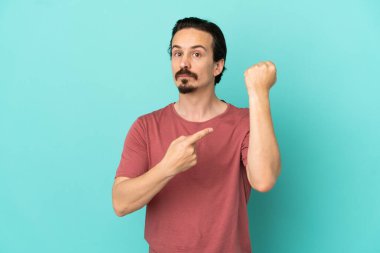 Kafkasyalı genç adam mavi arka planda izole edilmiş. Geç kalma jesti yapıyor.