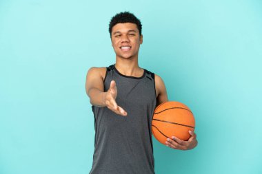 Basketball player African American man isolated on blue background shaking hands for closing a good deal