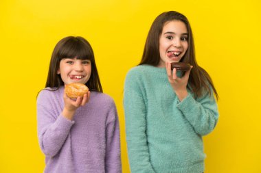 Sarı arka planda izole edilmiş küçük kız kardeşler ellerinde donut tutuyorlar.