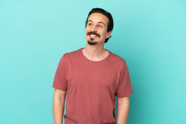 Kafkasyalı genç adam mavi arka planda izole edilmiş bir şekilde yukarı bakarken bir fikir düşünüyor.