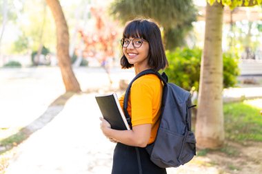 Parkta elinde mutlu bir ifadeyle not defteri tutan genç bir kız öğrenci.