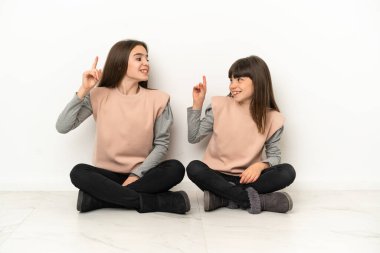 Beyaz arka planda izole bir şekilde yerde oturan küçük kız kardeşler, bir parmağını kaldırarak çözümü anlamaya çalışıyorlar.