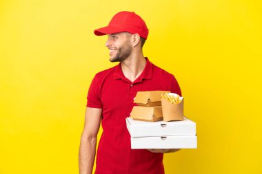 Pizza teslimatçısı pizza kutularını ve hamburgerleri alıp arka planda gülüyor.