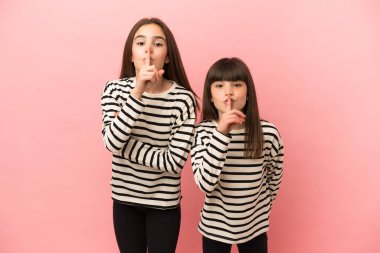 Pembe arka planda izole edilmiş küçük kız kardeşler sessizlik işareti gösteriyor. Parmağını ağzına sok.