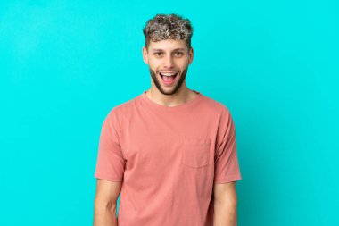 Mavi arka planda mahsur kalmış yakışıklı, beyaz bir adam. Şaşırtıcı bir yüz ifadesi var.