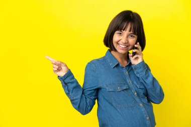 Sarı arka planda izole edilmiş cep telefonu kullanan hamile bir kadın var.
