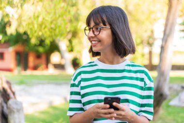 Parktaki genç esmer kadın cep telefonu kullanıyor.