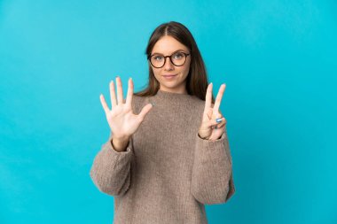 Genç Litvanyalı kadın mavi arka planda izole edilmiş. Parmakları olan yediyi sayıyor.