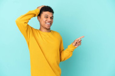 Genç Afro-Amerikalı adam mavi arka planda izole edildi. Şaşırdı ve işaret etti.