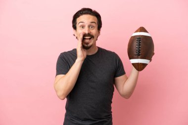 Pembe arka planda izole bir şekilde ragbi oynayan beyaz bir adam ağzı açık bağırıyor.