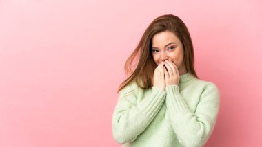 Soyutlanmış pembe arka planda genç bir kız mutlu ve gülümsüyor elleriyle ağzını kapatıyor.