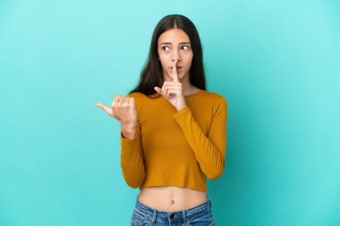 Mavi arka planda izole edilmiş genç bir Fransız kadın yan tarafı işaret ediyor ve sessiz hareketler yapıyor.