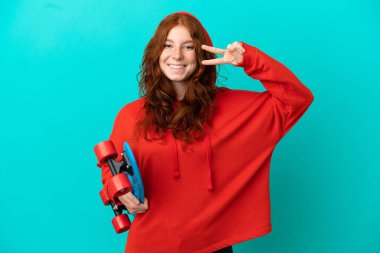 Genç kızıl saçlı kız mutlu bir ifadeyle mavi arka planda izole edilmiş.