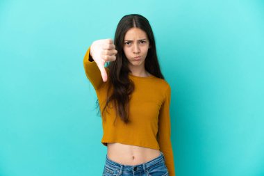 Mavi arka planda izole edilmiş genç bir Fransız kadın baş parmağını negatif ifadeyle aşağı gösteriyor.