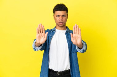 Genç Afrikalı Amerikalı adam sarı arka planda izole edilmiş. Durma hareketi yapıyor ve hayal kırıklığına uğruyor.