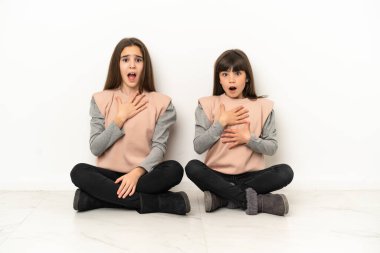 Beyaz arka planda izole edilmiş yerde oturan küçük kız kardeşler şaşırmış ve şok olmuştu.