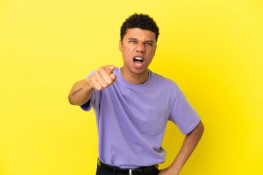 Sarı arka planda izole edilmiş genç Afrikalı Amerikalı hayal kırıklığına uğramış ve ön tarafı işaret ediyor.