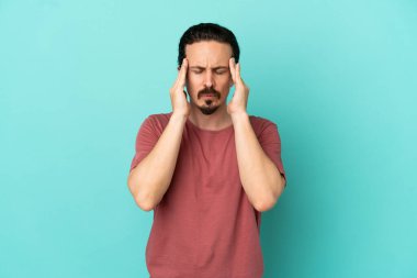 Kafkasyalı genç adam mavi arka planda izole edilmiş, baş ağrısı var.