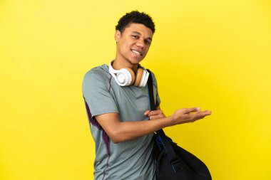 Young sport African American man with sport bag isolated on yellow background presenting an idea while looking smiling towards