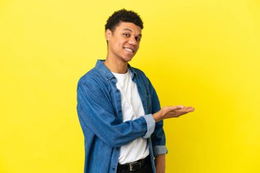 Genç Afrikalı Amerikalı adam sarı arka planda izole edilmiş bir şekilde gülümserken bir fikir sunuyor.