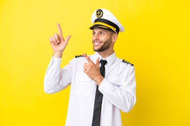 Kafkasyalı uçak pilotu sarı arka planda izole edilmiş işaret parmağıyla işaret etmek harika bir fikir.